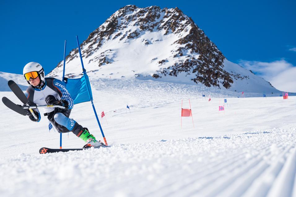 Skirennfahrer beim Slalom vor einer schneebedeckten Berglandschaft, umgeben von Toren auf der Piste.